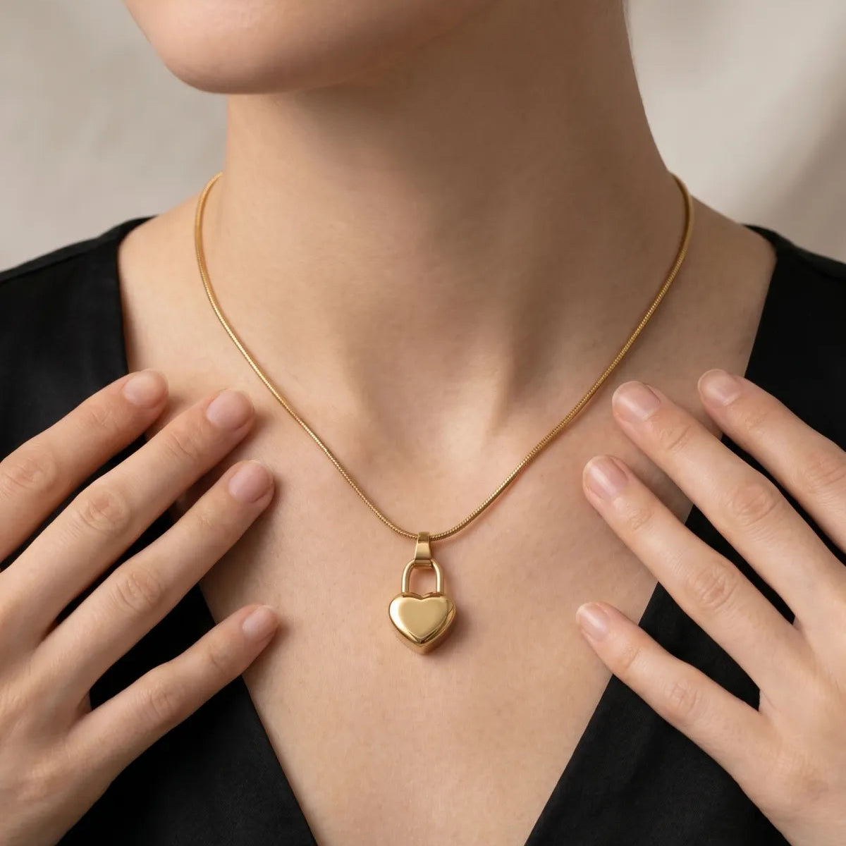 Gold necklace with a heart-shaped padlock pendant worn by a person against a neutral background