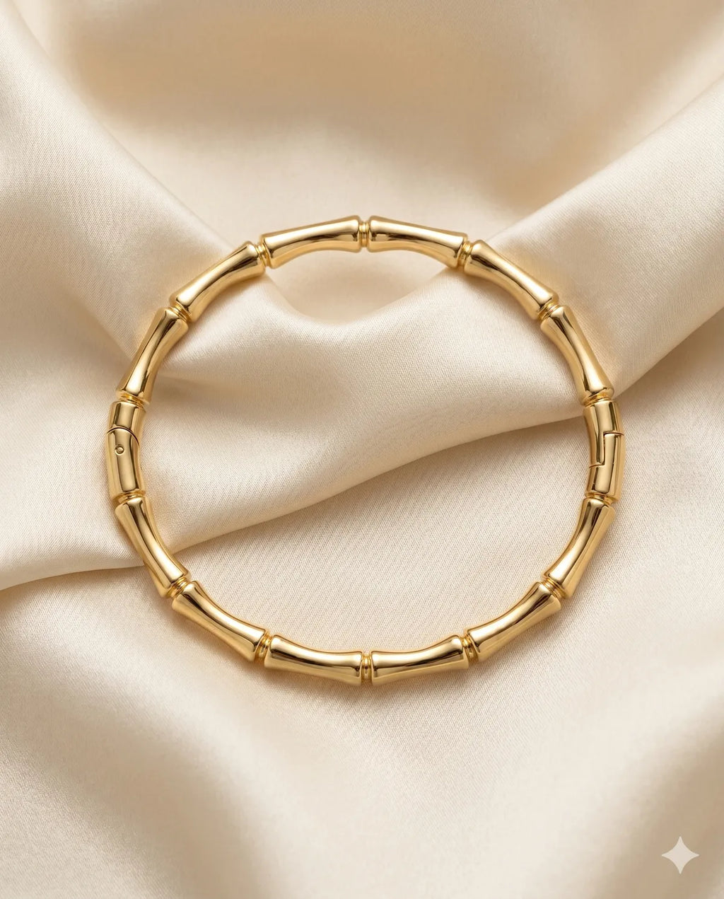 A gold-toned bangle bracelet designed to look like a segmented bamboo stalk, displayed on a draped cream satin fabric background.